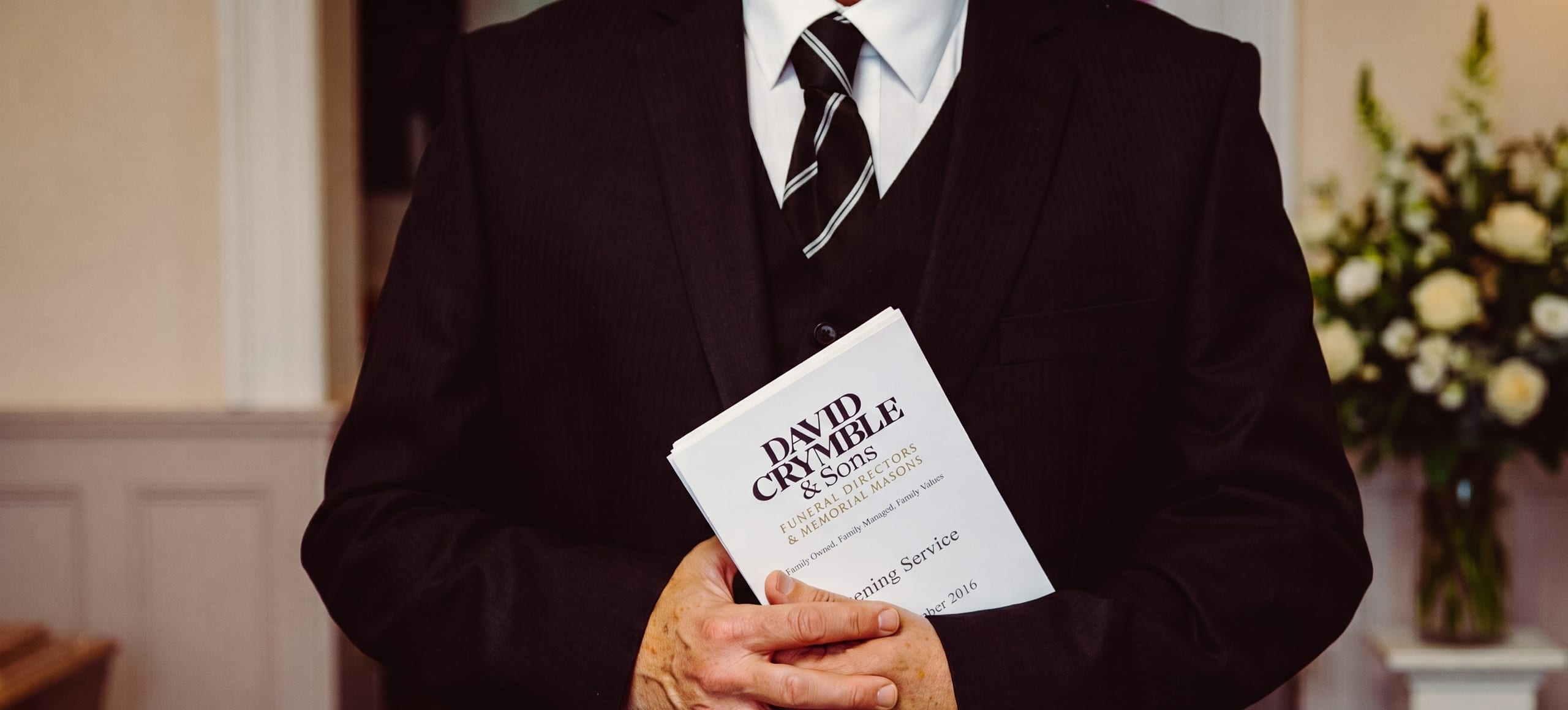 A funeral director from David Crymble & Sons holding an order of service.